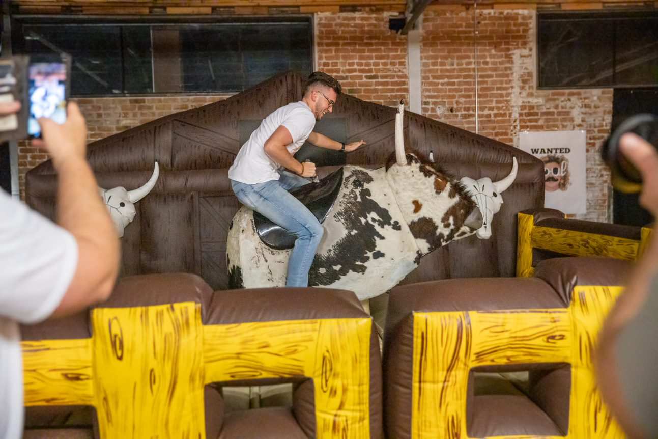 Guest riding a mechanical bull at a warehouse birthday party, brick wall behind