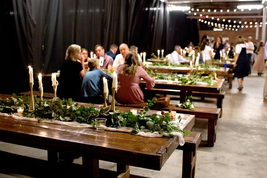 Long dinner tables set beneath string lights inside the warehouse