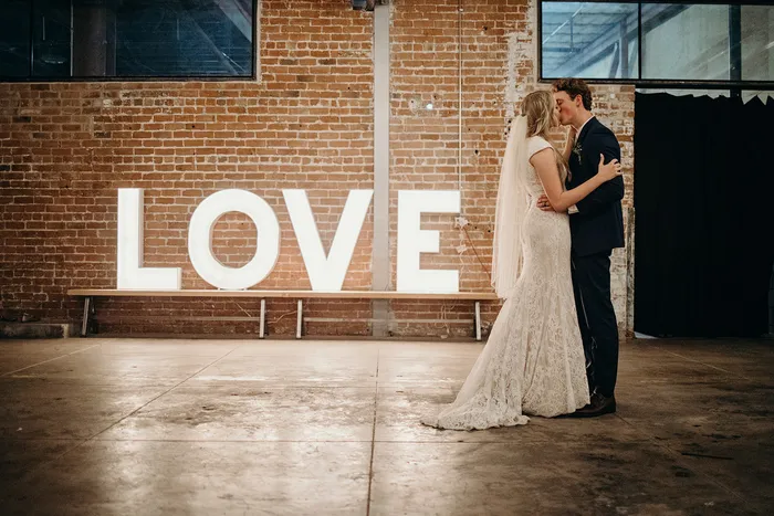 Couple beside marquee LOVE letters against original brick