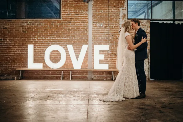 Bride and groom beside marquee LOVE letters against the brick wall