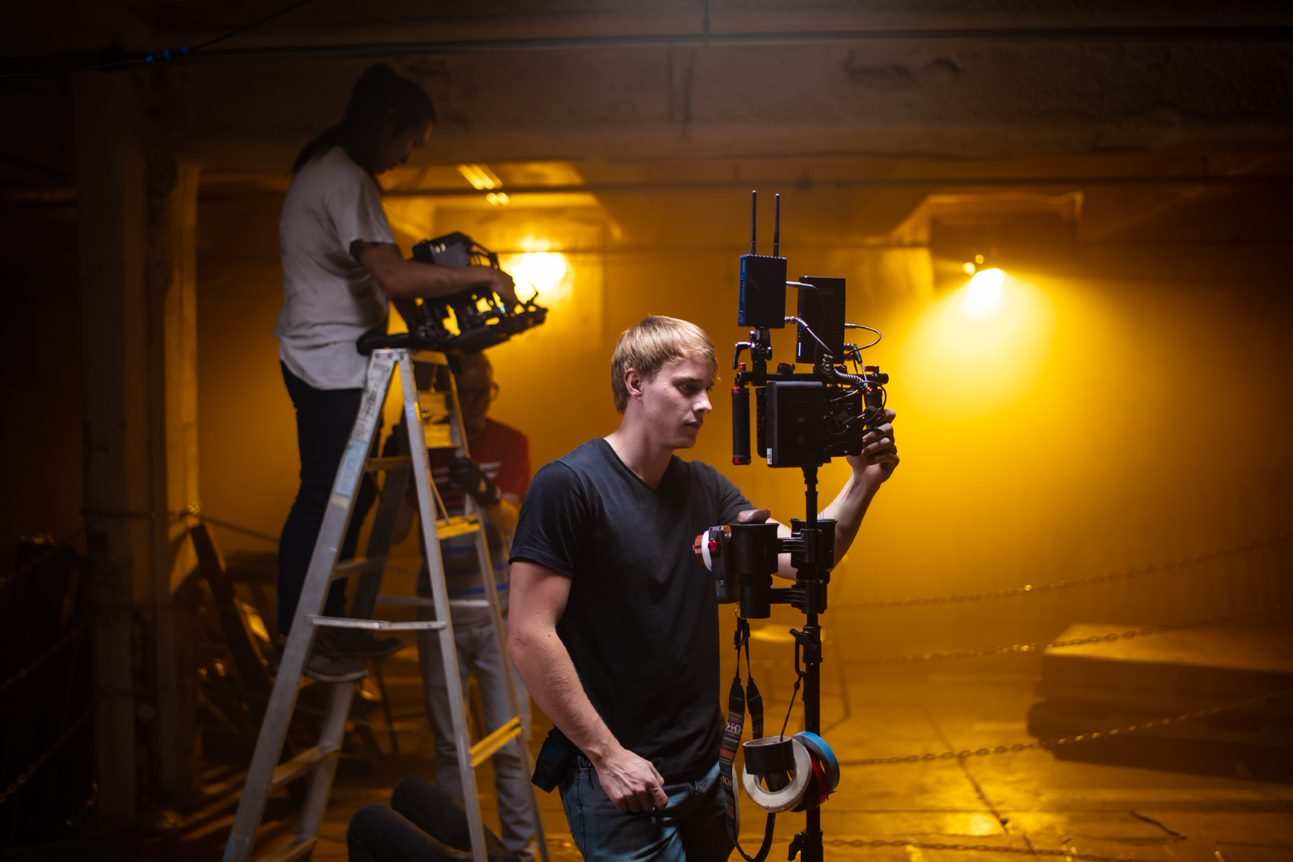 Film crew working camera rigs under amber lighting inside the warehouse