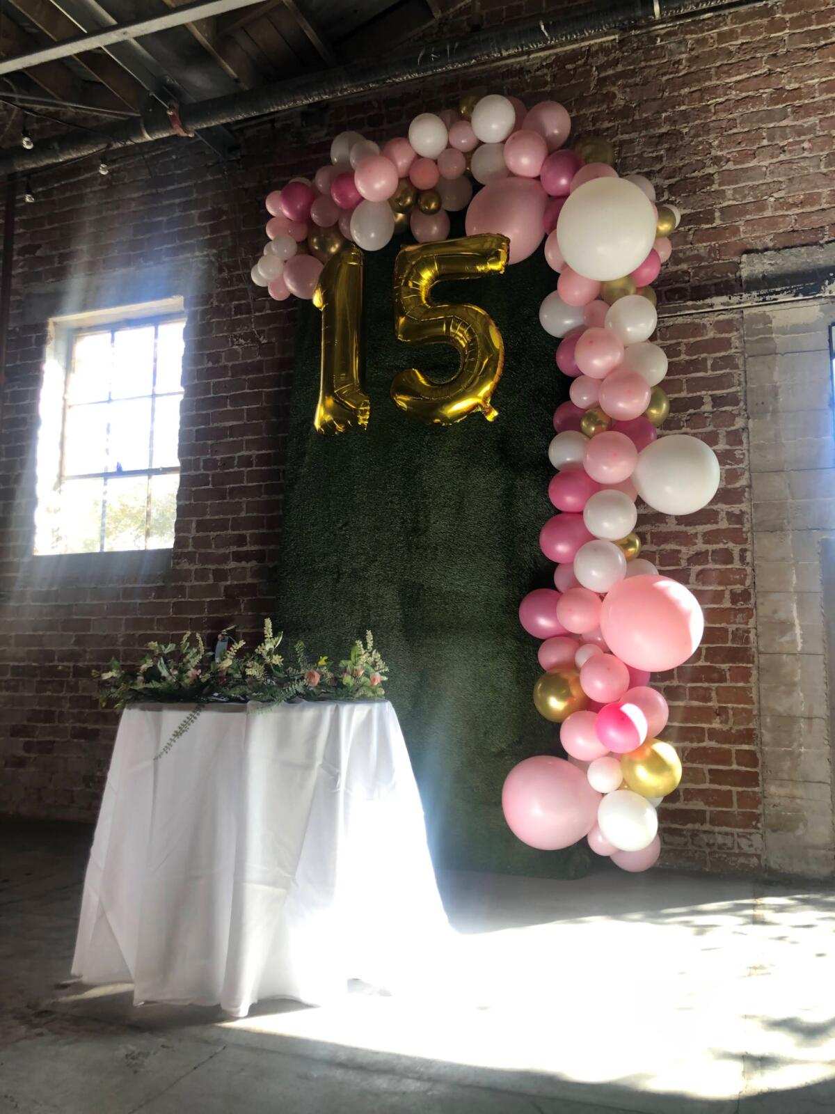 Quinceañera balloon arch in pink, white, and gold with a 15 marquee against the brick wall