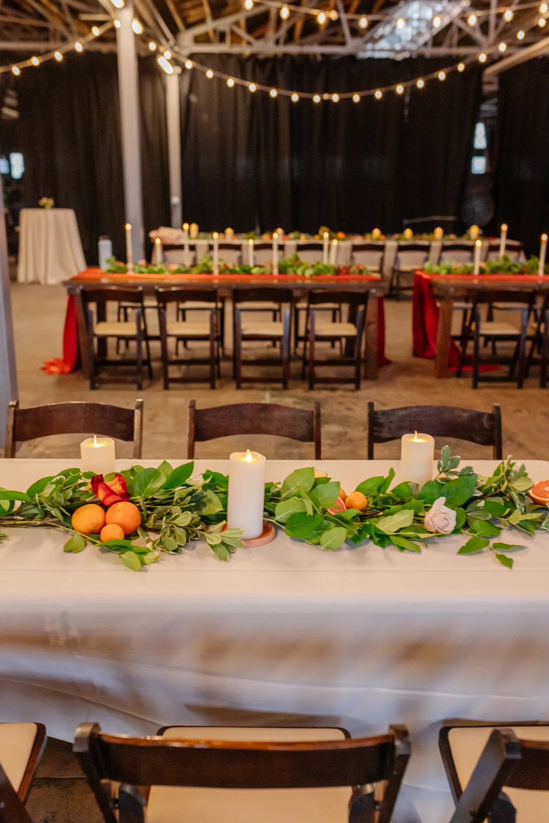 Reception head table with citrus-and-greenery garland and floral arrangements