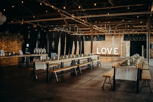 Reception tables under string lights with marquee LOVE letters across the warehouse floor