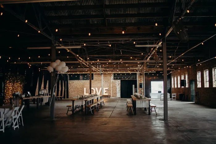 Long reception tables with marquee LOVE letters and balloons across the warehouse