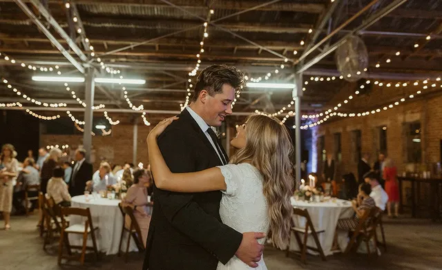 Couple's first dance under string lights, guests seated at round tables